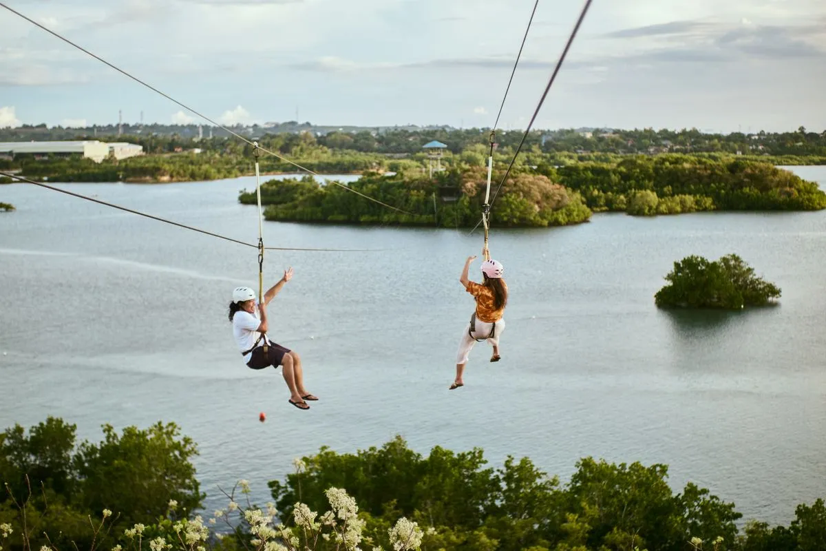 Two people on a zip line over calm water.